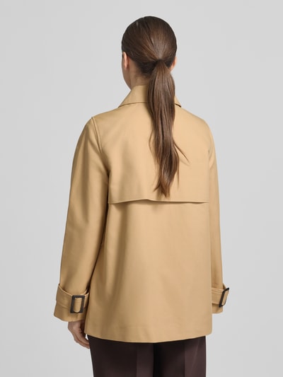 Frauenmodel trägt Trenchcoat mit Ärmelriegeln von Stefanel aus reiner Baumwolle in Beige, Zweireiher, ganzkörper Rückansicht.