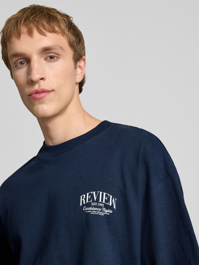 Männermodel trägt T-Shirt mit Label-Detail von REVIEW in Dunkelblau, Reine Baumwolle, Lockerer-Schnitt, Rundhalsausschnitt, 1/2-Arm, Nahaufnahme Oberkörper. Rückenlänge bei Größe M: 68 cm.