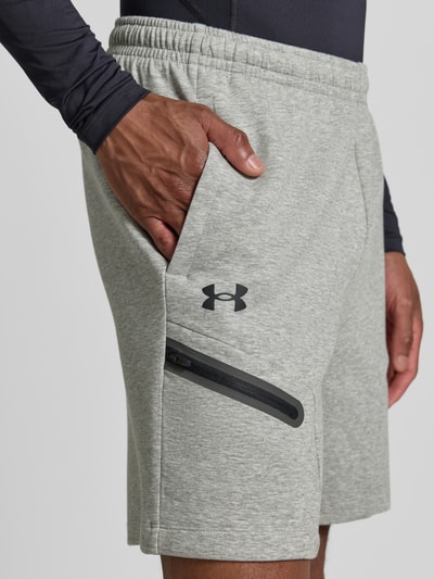 Männermodel trägt Shorts mit Reißverschlusstasche von Under Armour in Hellgrau, Material-Mix mit Baumwoll-Anteil, Logo, Regular-Fit, elastischer Bund, Detailaufnahme Oberschenkel.