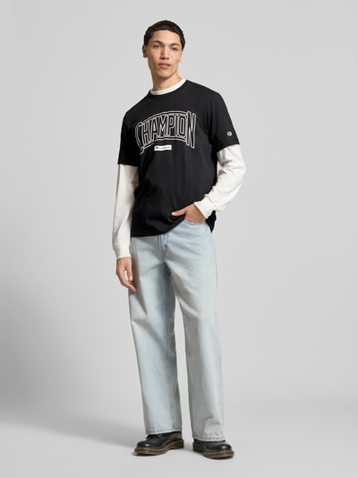 Männermodel trägt T-Shirt mit Logo und Rundhalsausschnitt von CHAMPION aus Reine Baumwolle im Regular-Fit, Vorderansicht Ganzkörperansicht.