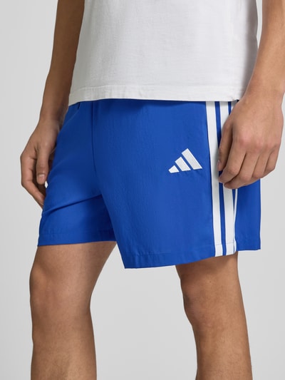 Männermodel trägt Regular Fit Sport-Shorts mit Tunnelzug von adidas Sportswear in Optik: Unifarben mit Logo-Print, Kontraststreifen, seitliche Eingrifftaschen, elastischer Bundabschluss, Detailaufnahme Oberschenkel.