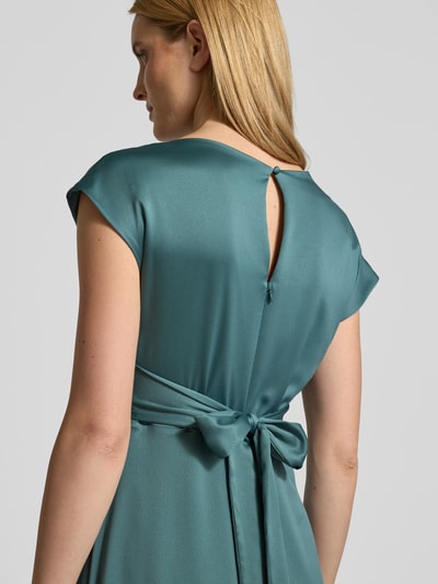 Frauenmodel trägt Relaxed Fit Midikleid mit Stoffband von Christian Berg Cocktail in Satin, kurzärmelig, matt schimmernd, Detailaufnahme Rückenansicht.