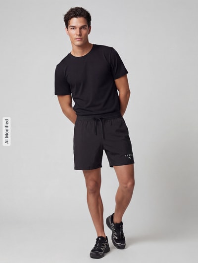 Männermodel trägt Regular Fit Sportshorts mit Label-Print von PUMA Performance in Schwarz, schlichtes Design, Ganzkörperansicht von vorne.
