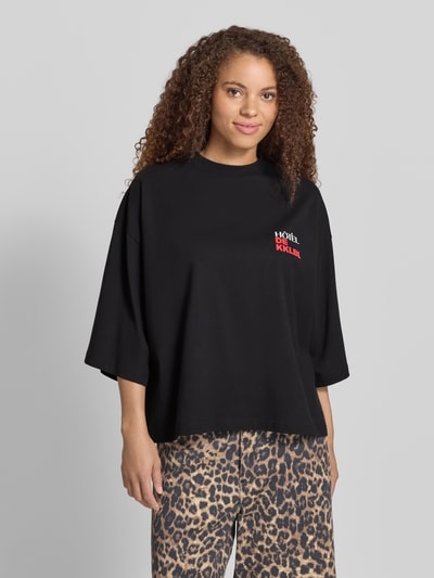Frauenmodel trägt Damen T-Shirt Cropped T-Shirt mit Statement-Print Modell 'Vacation' von Karo Kauer in Schwarz, Oversized-Fit, Reine Baumwolle, gerippter Rundhalsausschnitt, Vorderseite mit Statement-Print, Rückenlänge bei Größe S 62 cm, Ganzkörperansicht von vorne.