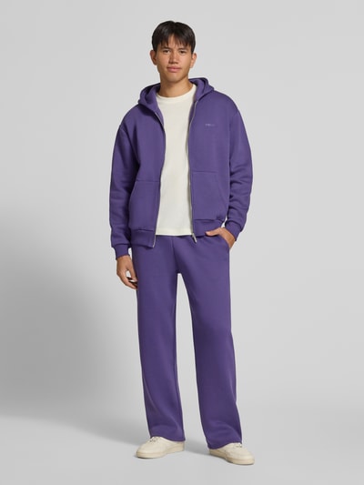 Männermodel trägt Straight Fit Sweatpants aus Baumwoll-Mix mit Label-Detail von REVIEW in Lila, Struktur weich, Ganzkörperansicht von vorne, Herren Sweatpants, elastischer Bund, Eingrifftaschen, Innenbeinlänge Größe M 80 cm