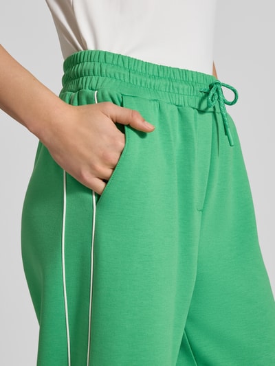 Kobiecy model nosi zielone spodnie dresowe z elastycznym pasem, model 'KATE NEO' od ICHI, mieszanka materiałów z dodatkiem wiskozy, krój wide fit, tunel, szerokość w rozmiarze S: 37 cm, długość wewnętrzna nogawki w rozmiarze S: 76 cm, zbliżenie na biodra