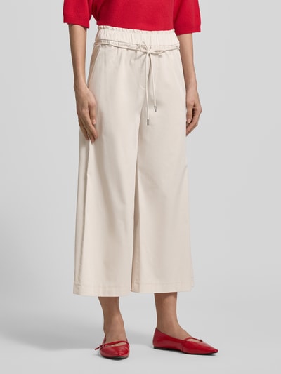 Vrouwenmodel draagt Culotte met elastische tailleband en bindriem van Marc Cain, katoenmix met viscose, wijde pijp, binnenbeenlengte 61 cm, bundwijdte 36 cm, lichte crème kleur, gladde textuur, detailopname onderlichaam, voorkant.