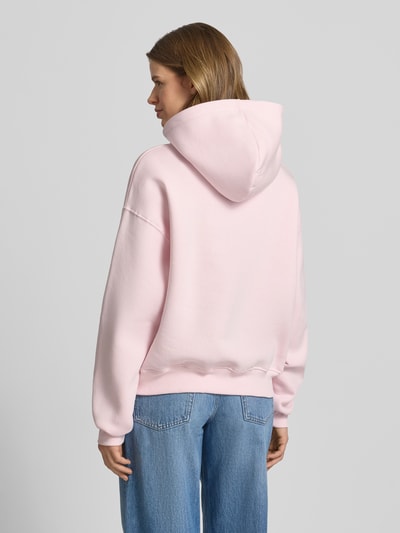Vrouwenmodel draagt Regular Fit Hoodie met kangoeroezak model 'Iconic' van Gina Tricot in lichtroze katoenmix, elastische boorden. Volledige lichaamsopname achteraan.