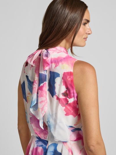 Vrouwenmodel draagt cocktailjurk met asymmetrische zoom van Vera Mont in kleurrijk bloemenpatroon, opstaande kraag, druppelvormige hals met strik en rugritssluiting, getailleerd model, midi-jurk, ruglengte maat 36: 112 cm, borstwijdte maat 36: 40 cm. Detailopname rug.