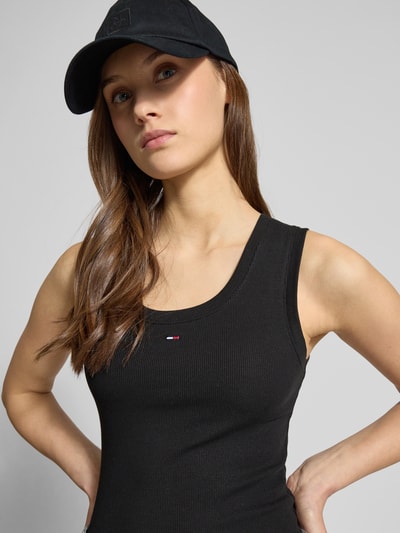 Modelka kobieca nosi Slim Fit Tank Top aus Baumwoll-Mix od Tommy Jeans, czarny, prążkowany, logo, szerokie ramiączka, u-neck, krój slim fit, detal logo, bawełniany miks, zbliżenie górnej części ciała.