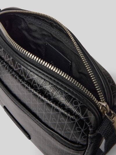 Produktfoto, Handtasche mit Logo-Muster und Schulterriemen von CK Calvin Klein, Hauptfach mit Reißverschluss, Label-Detail, schwarze Struktur, Maße: 22 cm Breite, 16 cm Länge, 5 cm Tiefe, Schulterriemen 106 cm, Herren Accessoire.
