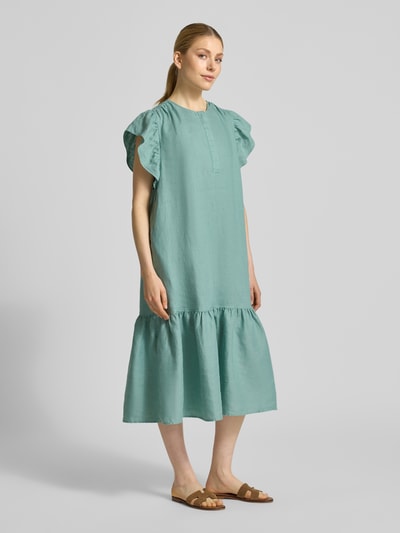 Modelka kobieca ma na sobie Leinenkleid mit Rüschen und Rundhalsausschnitt od Christian Berg Woman, czyste len, krój A-linii, długość midi, okrągły dekolt, falbany, długość tyłu w rozmiarze 36: 118 cm, szerokość w rozmiarze 36: 52 cm, długość rękawa w rozmiarze 36: 15 cm, miękka tekstura, matowy jasnoturkusowy odcień, całkowity widok z przodu.