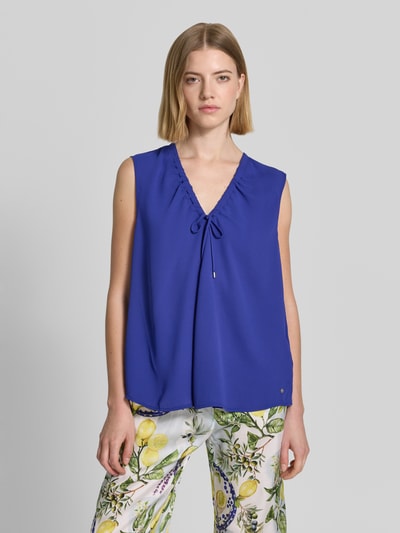 Kobiece modelka nosi Regular Fit Bluse mit Zierschleife von Marc Cain, dekolt w serek, krój regular fit, ozdobna kokarda, tunel, bez rękawów, długość tyłu w rozmiarze 36: 62 cm, intensywny niebieski kolor, gładka faktura, przód bez wzoru, widok całej sylwetki z przodu.