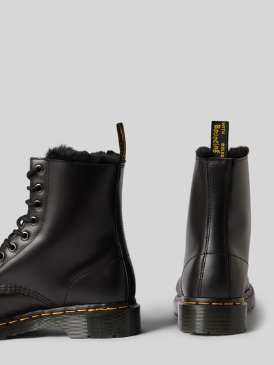 Produktfoto, schwarze Boots aus echtem Leder mit Label-Detail Modell 'Serena' von Dr. Martens, strukturierte Sohle, Schnürverschluss, abgerundete Spitze, sichtbare Nähte, kontrastierende gelbe Details, matter Look, Damen Schuhe, Absatzhöhe 4 cm, Schafthöhe 16 cm, Schaftweite 9 cm.