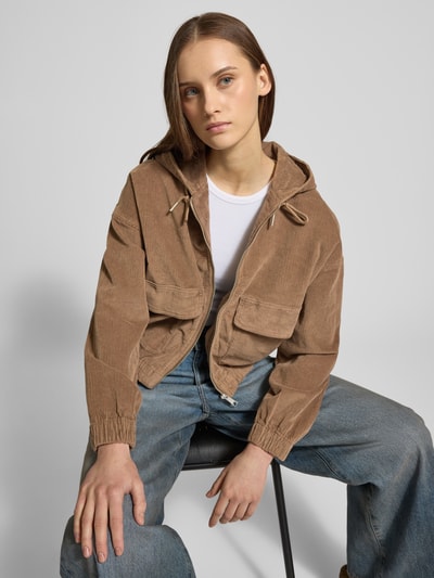 Kobiece modelka nosi Oversized Bomberjacke aus Baumwoll-Mix Modell 'KENZIE' od Only w kolorze brązowym, sztruks, duże kieszenie, kaptur, rozpinana, szeroki krój, widok na górną część ciała z przodu.