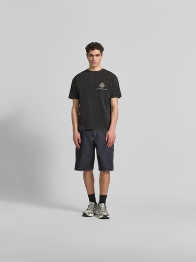 Männermodel trägt Relaxed Fit T-Shirt aus Baumwoll-Mix von Don´t Waste Culture in Schwarz mit Used-Look und Label-Details, Ganzkörperansicht von vorne. Rückenlänge bei Größe M: 68 cm.