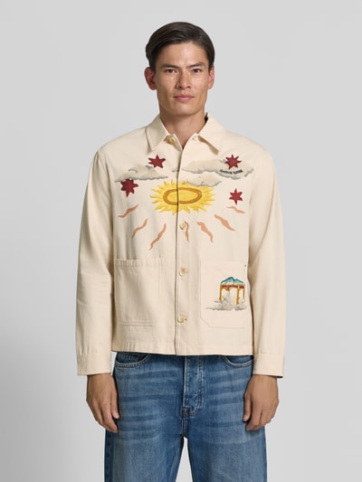 Männermodel trägt Regular Fit Overshirt mit Motiv-Prints- und -Applikationen von Scotch & Soda in Beige, reine Baumwolle, Ganzkörperansicht von vorne.