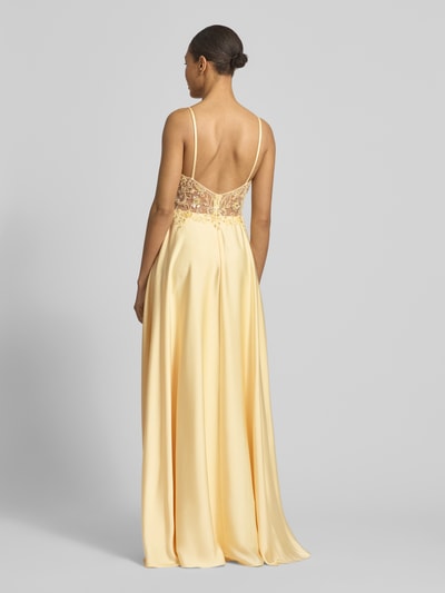 Modelka kobieca nosi Abendkleid mit floralem Ziersteinbesatz od Laona, żółty satynowy materiał, taliowany krój, półprzezroczysty tył z florystycznym zdobieniem z kamieni i cekinów, cienkie ramiączka, długość tyłu w rozmiarze 36: 124 cm, szerokość w rozmiarze 36: 30 cm, widok całej sylwetki z tyłu.