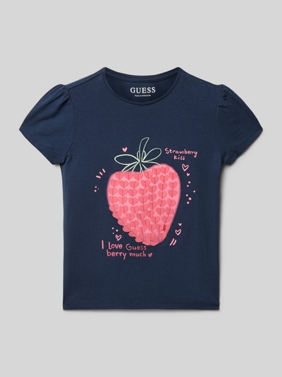 Mädchen trägt Regular Fit T-Shirt mit Zierbesatz von Guess in Dunkelblau mit Logo-Print und Rundhalsausschnitt, Nahaufnahme Oberkörper. Kinder T-Shirt aus elastischem Baumwoll-Mix, Rückenlänge bei Größe 116: 41 cm.