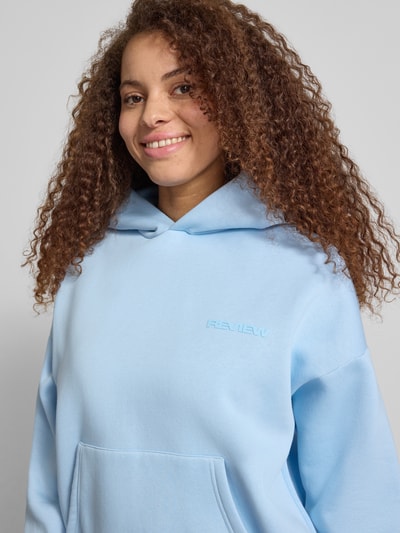 Frauenmodel trägt Hoodie mit Logo-Print und Känguru-Tasche von REVIEW in Hellblau, Baumwoll-Mix, Loose-Fit, Kapuze, Nahaufnahme Oberkörper.
