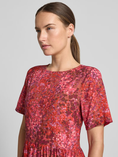 Frauenmodel trägt Midikleid aus Viskose im Allover-Look von Rich & Royal in Rot- und Rosatönen, Nahaufnahme Oberkörper, A-Linie, Rundhalsausschnitt, reine Viskose, Brustweite bei Größe 36: 47 cm, Ärmellänge 23 cm.