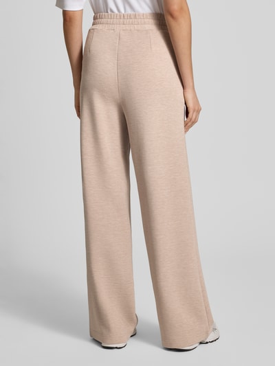 Kobieta nosi spodnie dresowe z szerokimi nogawkami Sweatpants mit weitem Bein und Eingrifftaschen od VARLEY, mieszanka wiskozy z dodatkiem streczu, elastyczny pas, wpuszczane kieszenie, model the extra wide leg pant 3, szerokość w pasie 36 cm, długość wewnętrzna nogawki 84 cm dla rozmiaru S, kolor beżowy, widok całej sylwetki z tyłu.