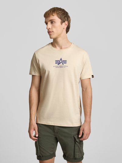 Männermodel trägt T-Shirt mit Logo und Rundhalsausschnitt von Alpha Industries, Beige, Reine Baumwolle, Regular-Fit, Vorderseite bedruckt, Ganzkörperansicht von vorne.