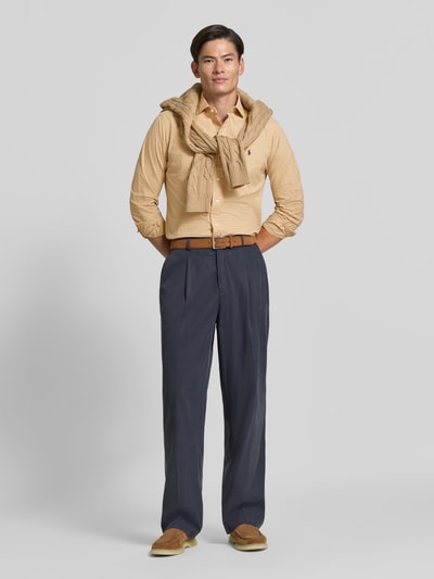 Männermodel trägt Custom Fit Freizeithemd aus reiner Baumwolle von Polo Ralph Lauren in Beige, kombiniert mit blauen Hosen, Ganzkörperansicht von vorne.