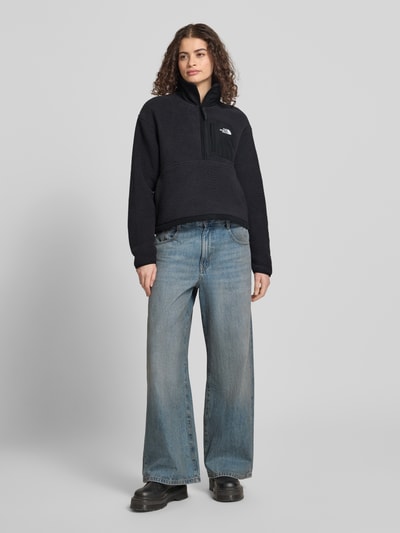 Frauenmodel trägt Fleecepullover mit Troyer-Kragen Modell 'YUMIORI' von The North Face in Schwarz, Label-Detail, Gerade Passform, Elastische Abschlüsse, Ganzkörperansicht von vorne. Rückenlänge bei Größe S: 54 cm, Schulterbreite: 51 cm, Brustweite: 56 cm, Ärmellänge: 58 cm.