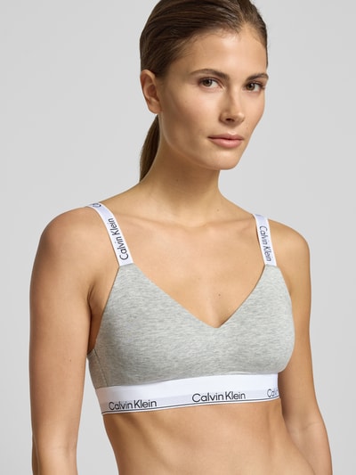 Modelka nosi Bralette mit Label-Bund od Calvin Klein Underwear, szarość, biały napis, dopasowany krój, zbliżenie na górną część ciała.