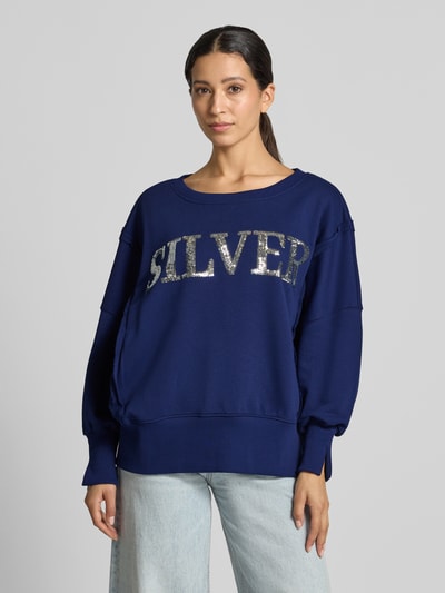 Frauenmodel trägt Oversized Sweatshirt aus reiner Baumwolle Modell 'Wide Silver' von miss goodlife in Dunkelblau mit Statement-Print, Paillettenbesatz und Rundhalsausschnitt, Ziernähte und elastische Abschlüsse, Nahaufnahme Oberkörper.