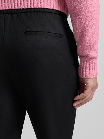 Männermodel trägt Slim Fit Stoffhose aus Lyocell-Mix Modell 'GETLIN251F3' von HUGO, schwarze Twill-Struktur, Detailaufnahme Rückansicht.