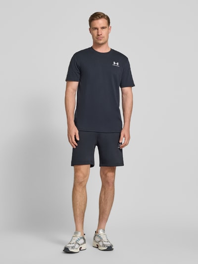 Männermodel trägt Regular Fit T-Shirt mit Logo-Stitching Modell 'Icon' von Under Armour aus Baumwoll-Mix, dunkel, Rundhalsausschnitt, Rückenlänge bei Größe M 72 cm, Ganzkörperansicht von vorne.