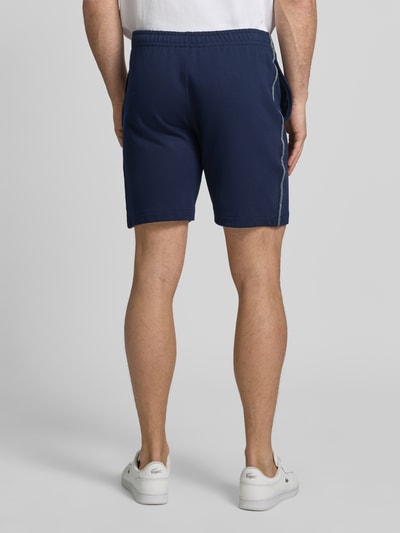 Männermodel trägt Regular Fit Sweatshorts aus reiner Baumwolle von Lacoste in Dunkelblau, Optik: Unifarben, Logostreifen, Bundabschluss elastisch mit Tunnelzug, 5-Pocket-Design, Gesäßtasche, Materialverarbeitung: Sweat, Ganzkörperansicht Rückansicht.
