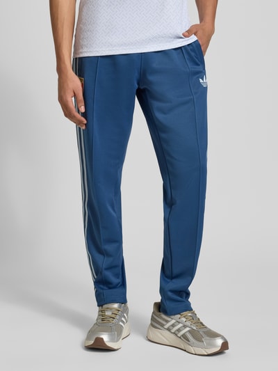 Mannenmodel draagt Regular Fit Sweatpants met katoenmodel 'FIGC OG' van adidas Originals, look: effen, regular fit, applicatie met labelstitching, contraststrepen, sluiting: tunnelkoord, boord: elastisch, materiaalverwerking: sweat, materiaal: materiaalmix met katoen, detailopname onderlichaam, vooraanzicht.