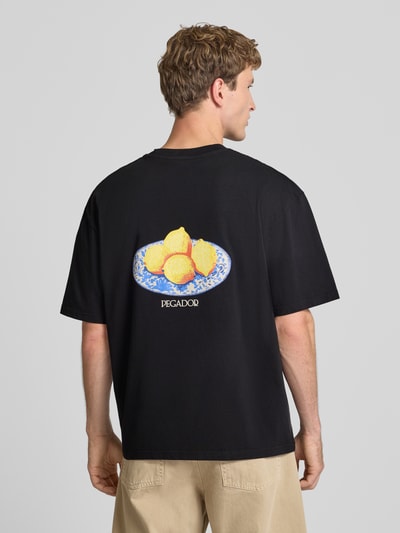 Männermodel trägt Oversized T-Shirt mit Backprint von PEGADOR in Schwarz, reine Baumwolle, Zitronen-Motiv, Rückenlänge 70 cm, Ganzkörperansicht Rückansicht.