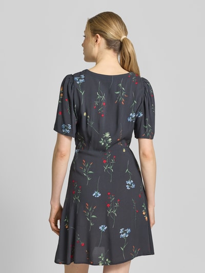 Frauenmodel trägt Leicht ausgestelltes Minikleid aus reiner Viskose Modell 'ALBA' von Vero Moda, Optik: Unifarben, Passform: Leicht ausgestellt, Länge: Mini, Ausschnitt: V-Ausschnitt, Details: Taillengürtel, Verschluss: Knopfleiste, Ärmelform: Kurzarm, Material: Reine Viskose, floral gemustert, Ganzkörperansicht Rückansicht.