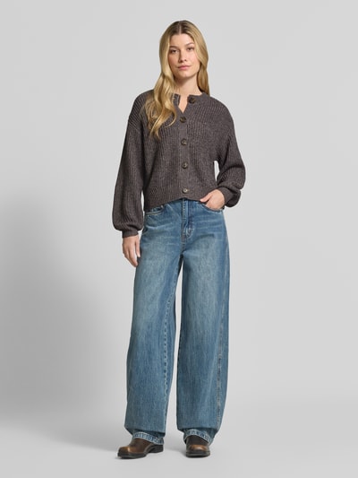 Frauenmodel trägt Loose Fit Strickjacke mit einreihiger Knopfleiste Modell 'LEA' von VERO MODA in Dunkelgrau, blaue Jeans, Ganzkörperansicht von vorne.