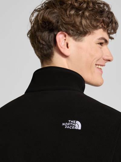 Männermodel trägt Fleecepullover mit Troyer-Kragen Modell 'GLACIER' von The North Face, fleece, rechte pasvorm, label-stitching, elastische boorden, ruglengte maat M 70 cm, mouwlengte maat M 72 cm, zwarte kleur, detailopname rug.