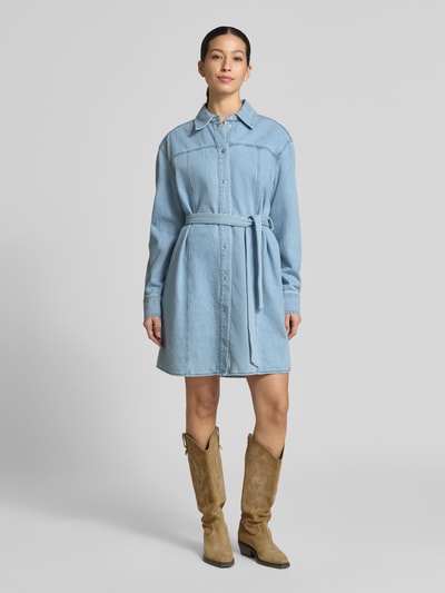 Vrouwenmodel draagt knielang denimjurk met overhemdkraag, strikceintuur, recht model van katoenmix, model 'Kimmia' van mbyM, frontaal volledige lichaamsopname.