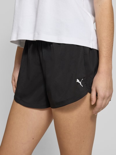 Frauenmodel trägt Regular Fit Shorts mit elastischem Bund von PUMA in Schwarz mit Logo-Print, ausgestellter Passform, Nahaufnahme Oberschenkel.