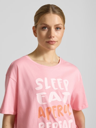 Frauenmodel trägt T-Shirt mit Motiv- und Statement-Print von Smith and Soul in Rosa, Rundhalsausschnitt, reine Baumwolle, Boxy Fit, Nahaufnahme Oberkörper.