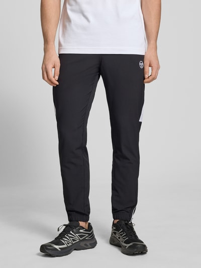 Männermodel trägt schwarze Sweatpants mit Logo-Stitching Modell 'CASPIO' von SERGIO TACCHINI, Material-Mix mit Stretch-Anteil, Körpernaher-Schnitt, Elastischer Bund mit Kordelzug, Seitliche Eingrifftaschen, Elastische Abschlüsse, Ganzkörperansicht von vorne.