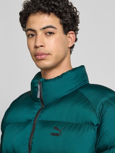 Männermodel trägt Steppjacke mit Label-Print von PUMA PERFORMANCE in Dunkelgrün, unifarben, Stehkragen, Nahaufnahme Oberkörper, reine Baumwolle