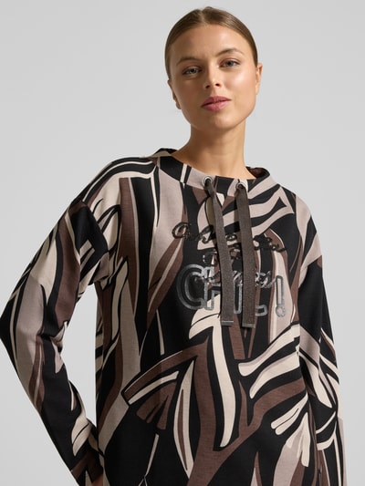 Modelka nosi Bluza 'Sweatshirt mit Tunnelzug' od Betty Barclay, mieszanka wiskozy z dodatkiem streczu, luźny krój, okrągły dekolt, tunel, detal z logo, brązowo-czarne abstrakcyjne wzory, wyrazista tekstura, widok z przodu, zbliżenie na górną część ciała.