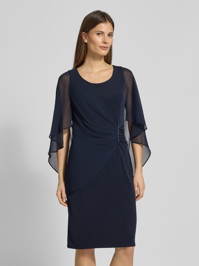 Frauenmodel trägt knielanges Cocktailkleid mit Rundhalsausschnitt von Vera Mont in Dunkelblau mit Fledermausärmeln aus Chiffon, Ganzkörperansicht von vorne. Elastischer Material-Mix, körpernahe Passform, Strasssteinbesatz, Rückseitiger Nahtreißverschluss.