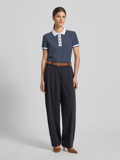 Kobiece model nosi koszulkę polo Cropped Poloshirt aus Viskose-Mix Modell 'ALPHONSINE' od Guess, mieszanka wiskozy z dodatkiem streczu, krój krótki, wzór w paski, listwa guzikowa, długość tyłu w rozmiarze S: 49 cm, widok całej sylwetki z przodu.