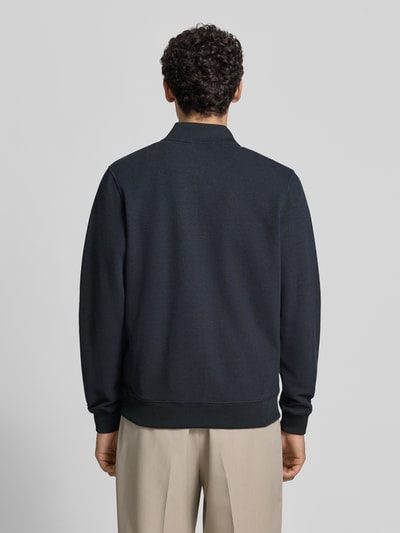 Männermodel trägt Sweatjacke mit Stehkragen von Christian Berg Men, dunkler Farbton, gerippte Abschlüsse, Material-Mix, Ganzkörperansicht Rückansicht.
