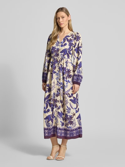 Frauenmodel trägt Midikleid aus Viskose-Mix Modell 'Sarai' von LOLLYS LAUNDRY mit violett-cremefarbenem Allover-Look, V-Ausschnitt, 3/4-Arm, A-Linie; Ganzkörperansicht von vorne. Rückenlänge 122 cm, Brustweite 41 cm, Ärmellänge 56 cm.