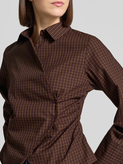 Frauenmodel trägt Bluse mit asymmetrischer Knopfleiste Modell 'Fenli' von Neo Noir, kariertes Muster in Braun und Gelb, Nahaufnahme Oberkörper, reine Baumwolle, Kentkragen, taillierter Schnitt, Kimonoärmel